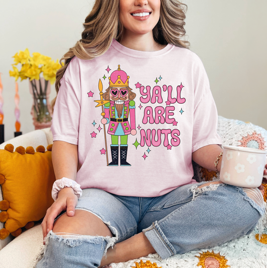 A woman wearing a pink t-shirt with a nutcracker character and the text "Ya'll are nuts" is sitting on a couch.