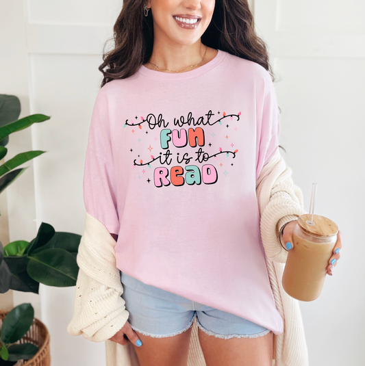 A woman wearing a pink t-shirt with a colorful text design and holding a drink.