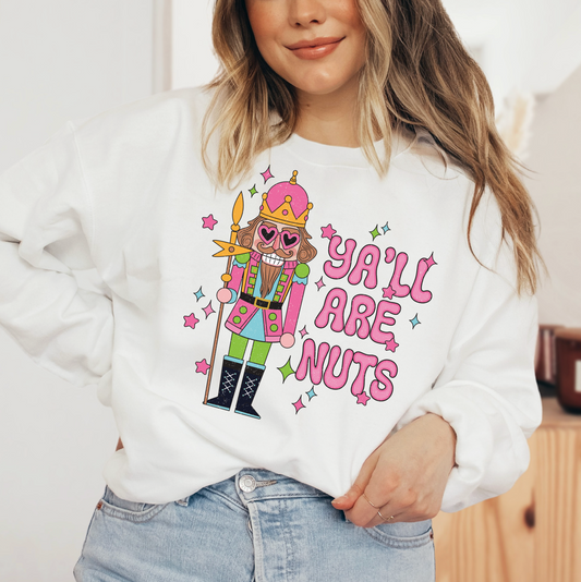 A woman wearing a white sweater with a colorful graphic design of a nutcracker character and the text "Ya'll are nuts" printed on it.