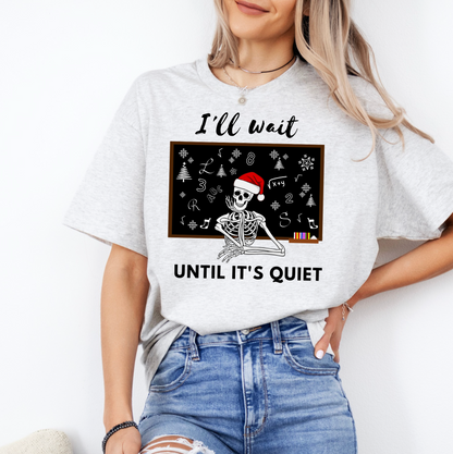 A woman wearing a white t-shirt with a graphic design of a skeleton wearing a Santa hat and the text "I'll wait until it's quiet" printed on it.
