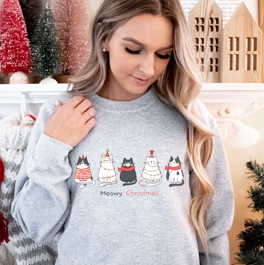 A woman wearing a grey sweatshirt with a graphic of five cats and the text "Meowy Christmas" printed on it.