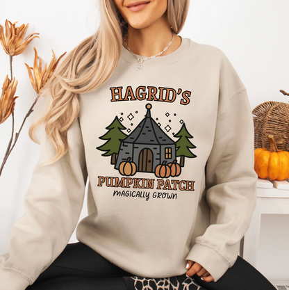A woman wearing a beige sweatshirt with a graphic design of a pumpkin patch and a castle, along with the text "Hagrid's Pumpkin Patch" and "magically grown".