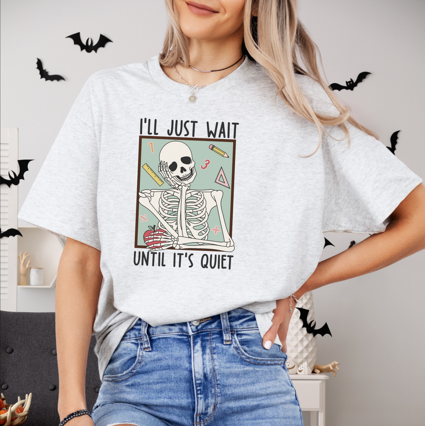 A woman wearing a white t-shirt with a graphic design of a skeleton and the text "I'll just wait until it's quiet" printed on it.