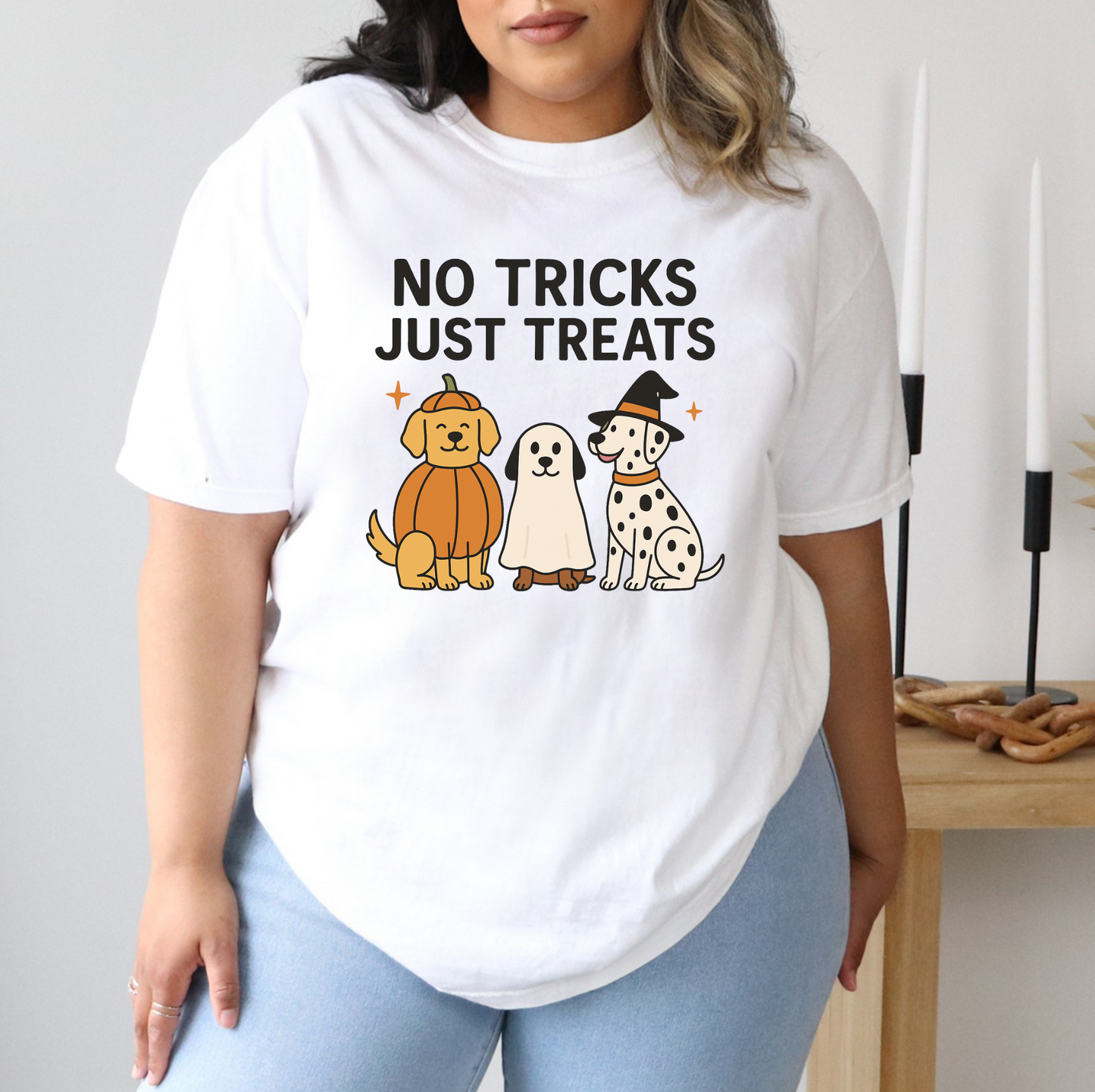 A person wearing a white t-shirt with a graphic design featuring three cartoon dogs and the text "NO TRICKS JUST TREATS".