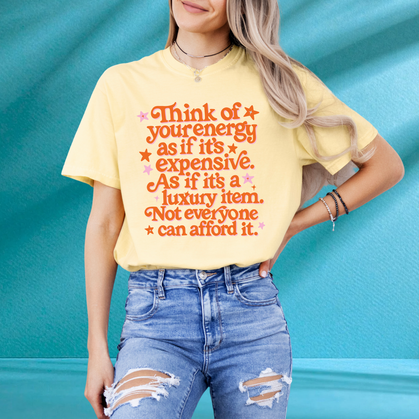 A woman wearing a yellow t-shirt with a printed message and ripped jeans stands against a blue background.