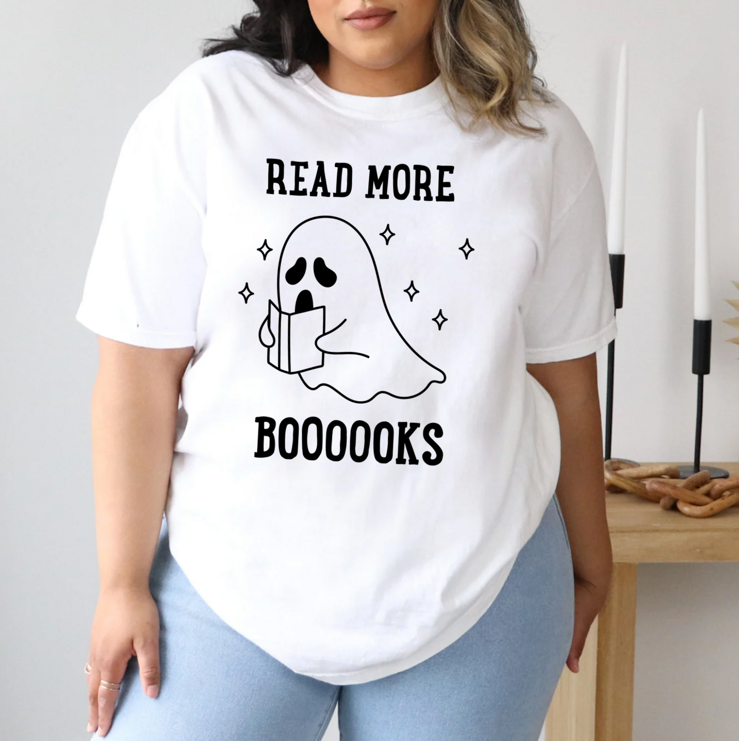 A person wearing a white t-shirt with a graphic design of a ghost holding a book and the text "Read more BOOOOKS" printed on it.