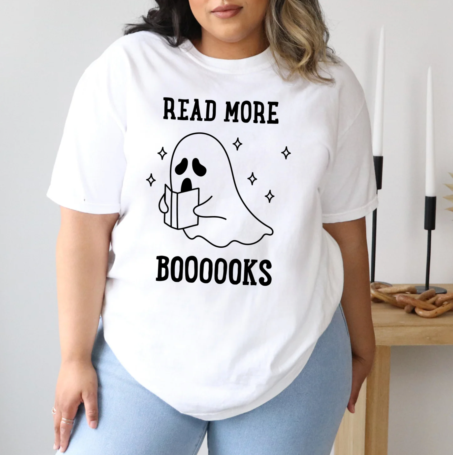 A person wearing a white t-shirt with a graphic design of a ghost holding a book and the text "Read more BOOOOKS" printed on it.