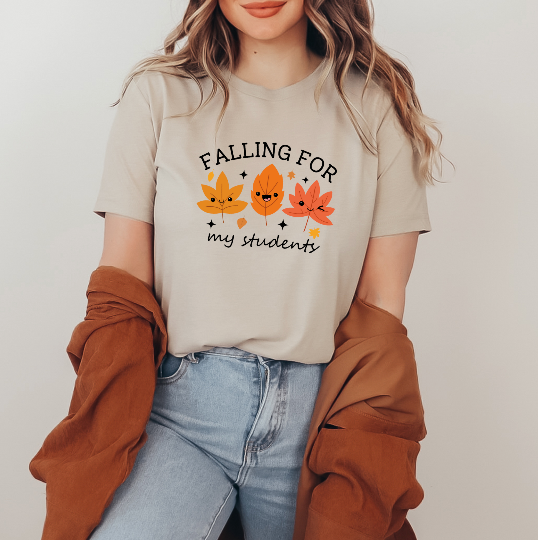 A woman wearing a beige t-shirt with a graphic design of three autumn leaves and the text "FALLING FOR my students" printed on it.