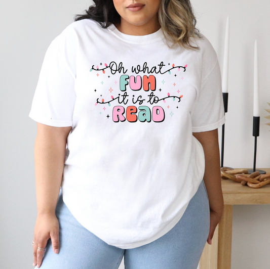 A person wearing a white t-shirt with a colorful graphic design that says "Oh what fun it is to read" in a playful font.