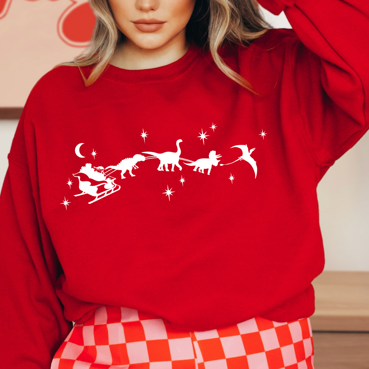 A woman wearing a red sweater with a white graphic design depicting a dinosaur sleigh ride with stars in the sky.