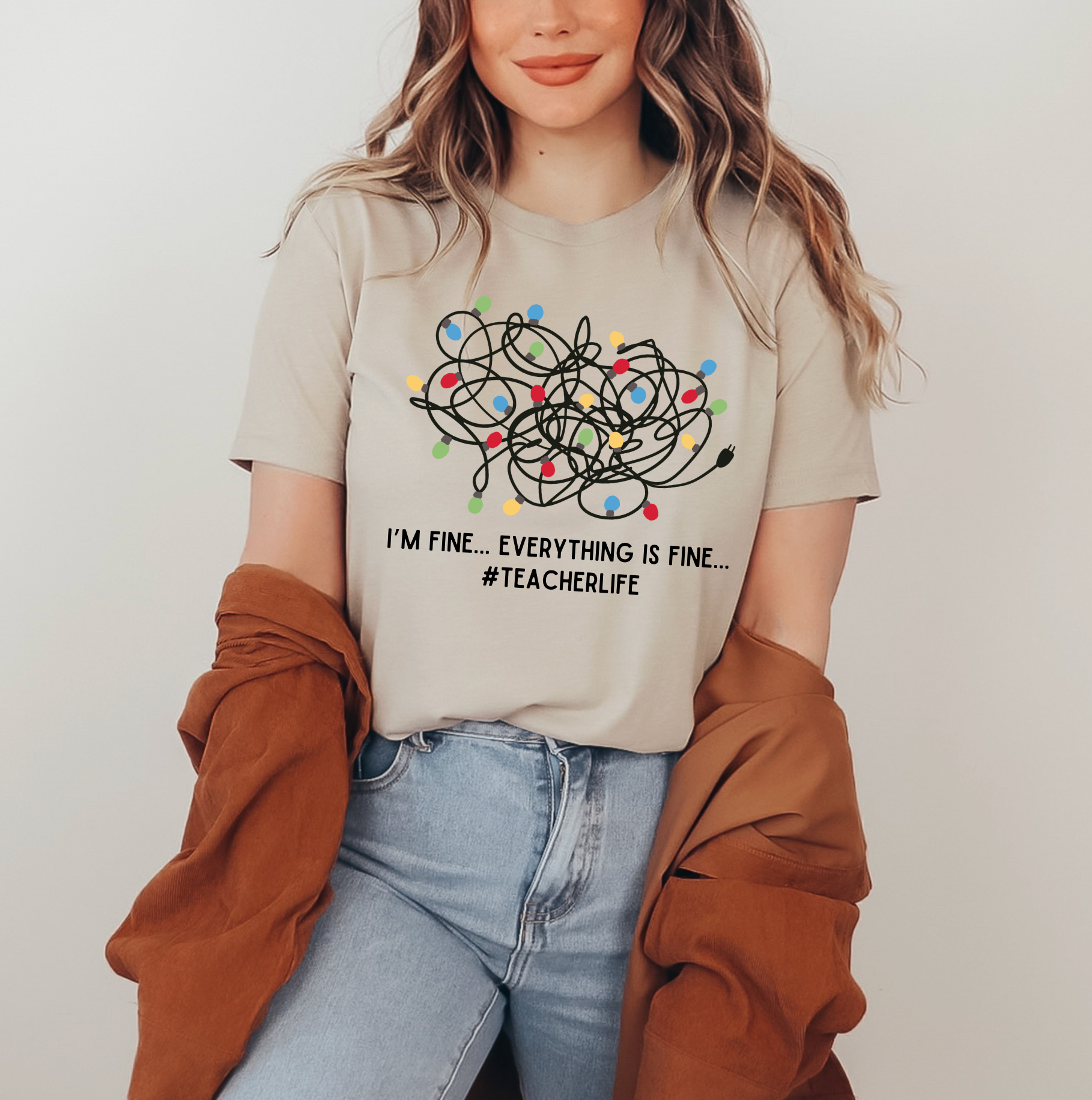 A woman wearing a beige t-shirt with a graphic design and text, standing against a white background.