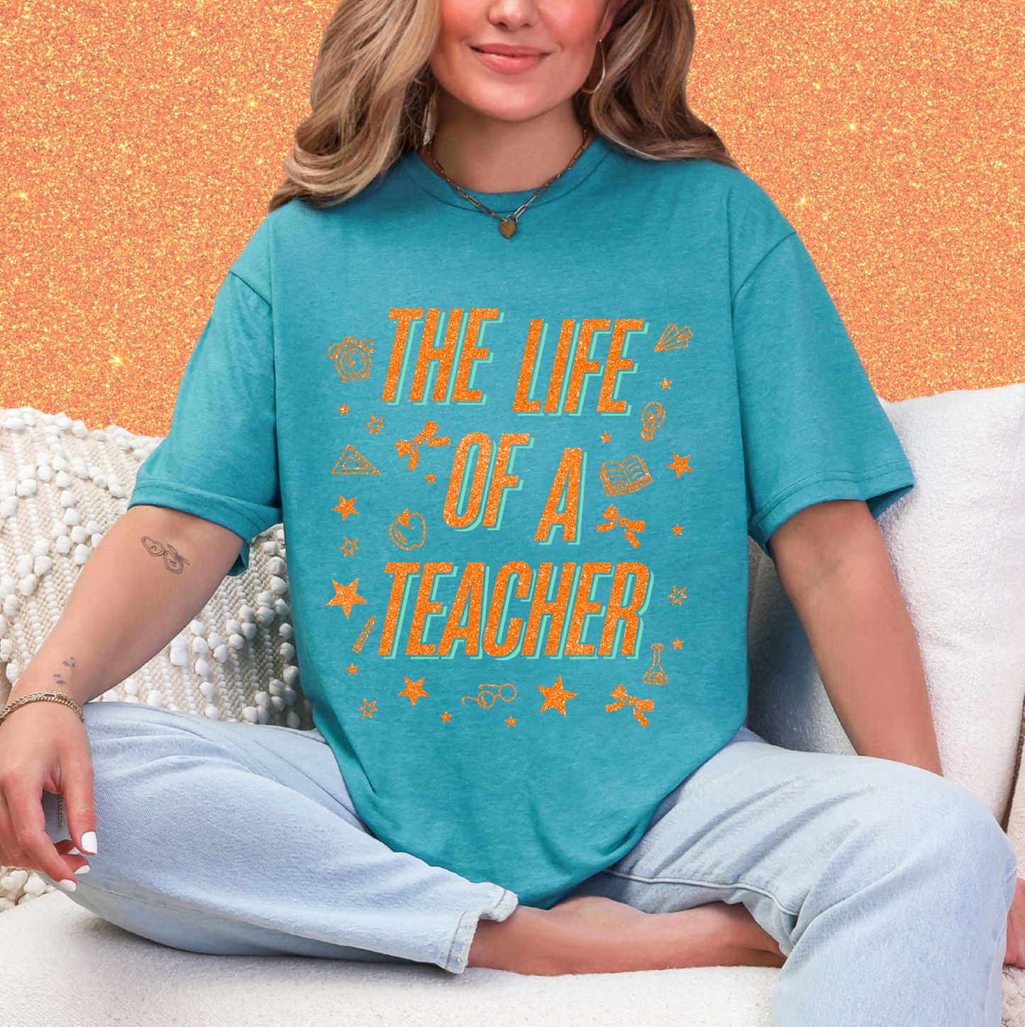 A woman wearing a teal t-shirt with the text "THE LIFE OF A TEACHER" printed on it, sitting on a couch.