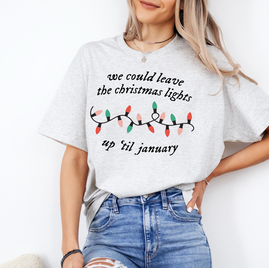 A woman wearing a grey t-shirt with a Christmas-themed design and text, standing against a white background.