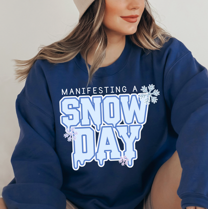 A woman wearing a blue sweatshirt with the text "MANIFESTING A SNOW DAY" printed on it.