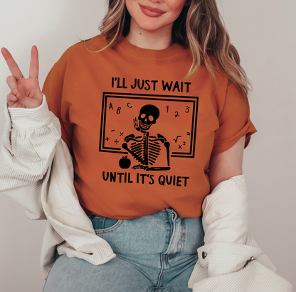 A woman wearing a t-shirt with a skeleton graphic and text, smiling and making a peace sign gesture.