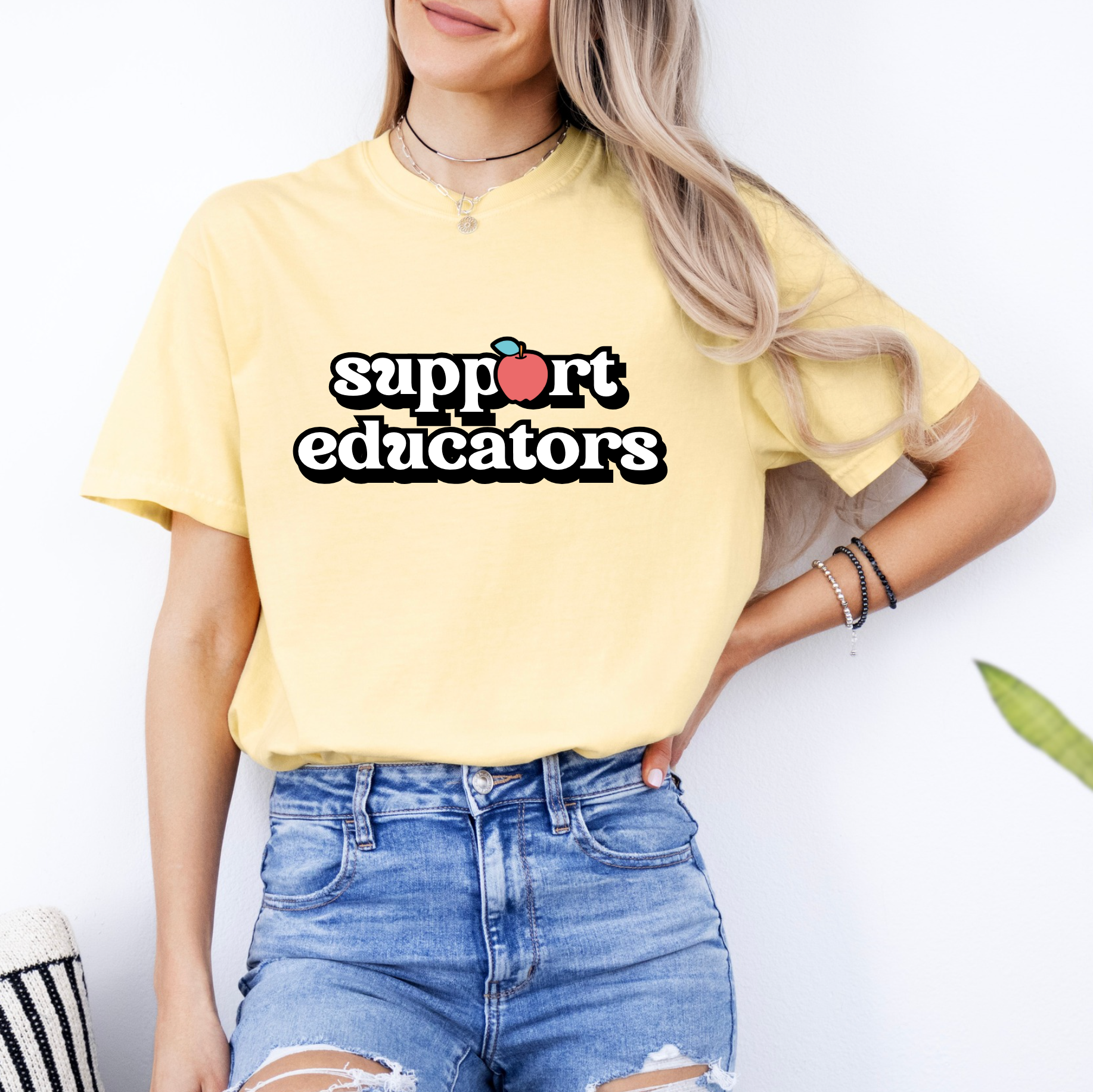 A woman wearing a yellow t-shirt with the text "support educators" printed on it, paired with distressed denim shorts.