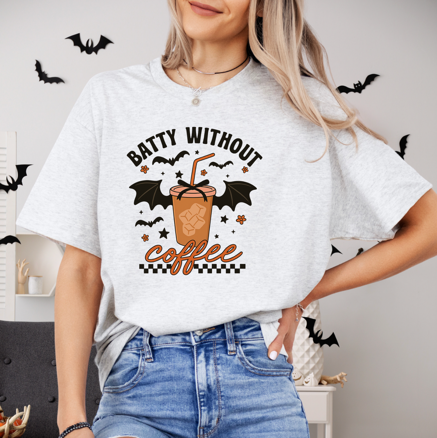 A woman wearing a white t-shirt with a graphic design of a bat-shaped coffee cup and the text "Batty without coffee" printed on it.