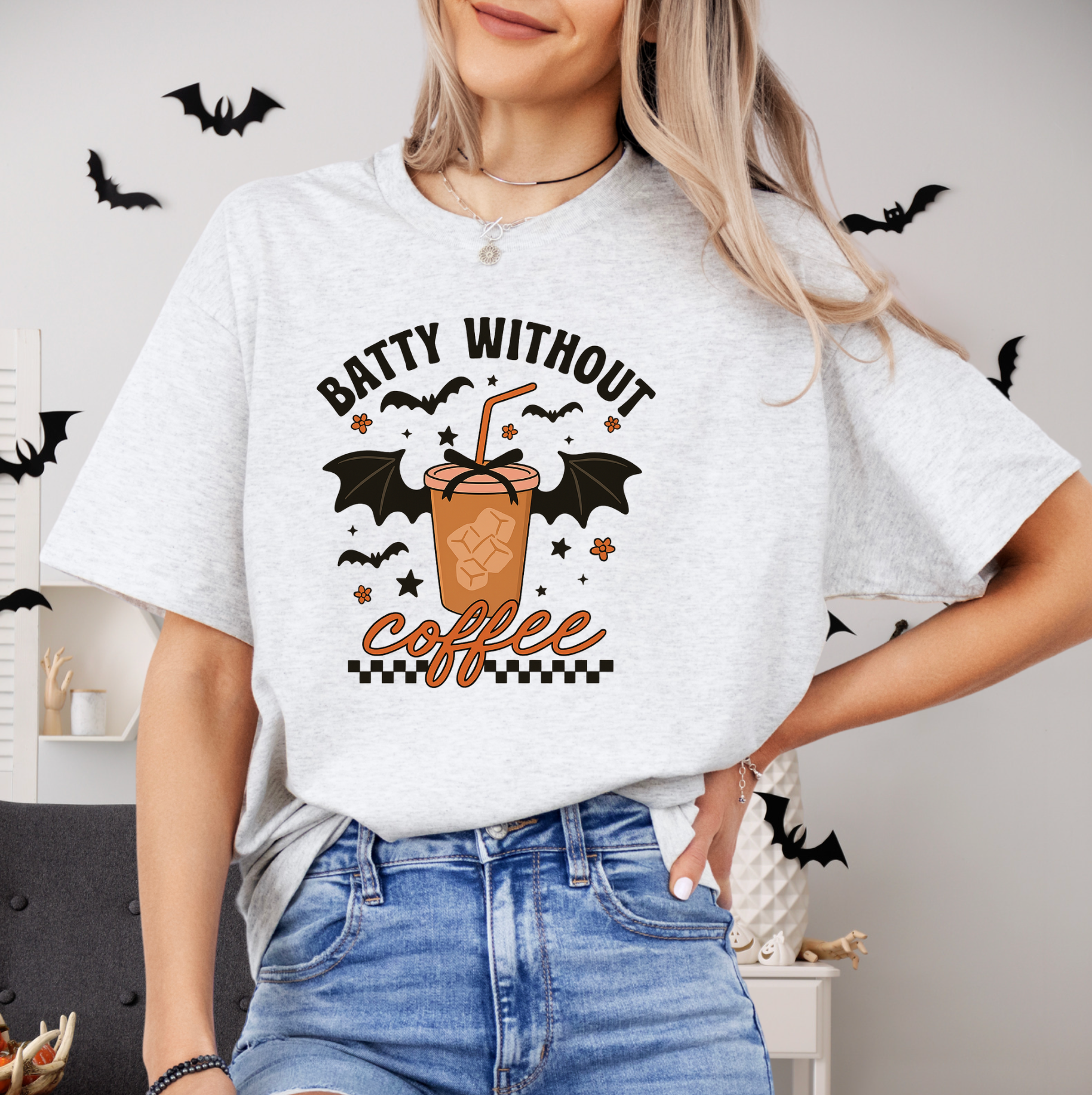A woman wearing a white t-shirt with a graphic design of a bat-shaped coffee cup and the text "Batty without coffee" printed on it.