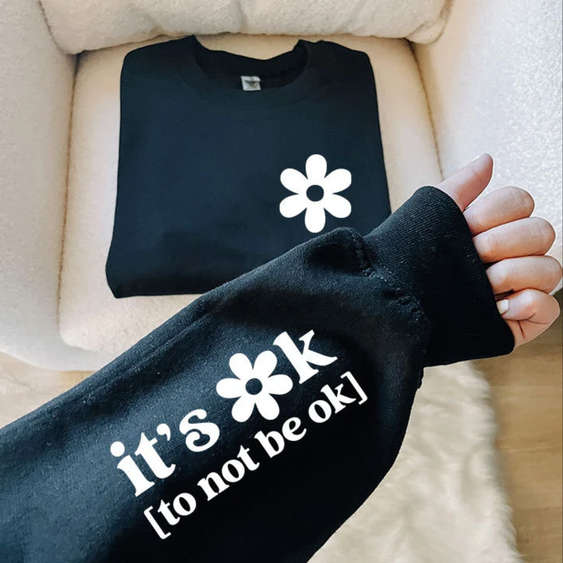 A person's arm wearing a black sweatshirt with the text "it's ok [to not be ok]" printed on it.